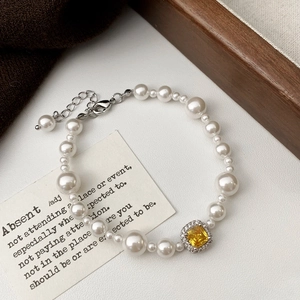 Détail de bracelet de perles avec pierre centrale jaune et diamants pavés