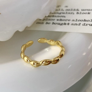 Detailed view of a golden olive-shaped beaded adjustable ring on a minimalist background