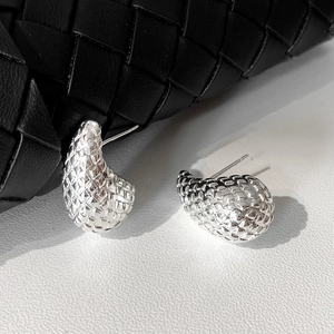 Macro shot of silver teardrop stud earrings with woven texture on black leather bag