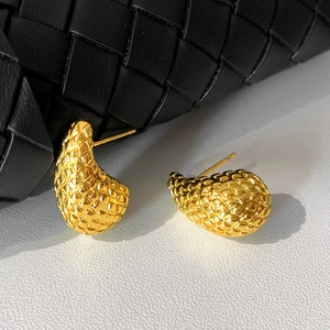 Close-up of gold teardrop earrings with woven texture next to a black leather bag