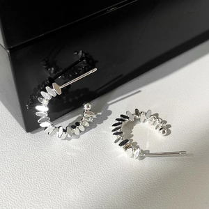 Macro detail of silver C-shaped textured earrings with layered oval metal pieces