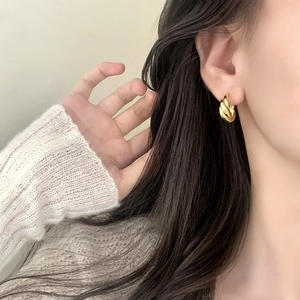 Eleganti orecchini a cerchio intrecciati dorati indossati da una modella in primo piano