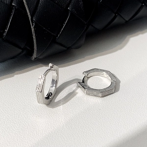 Close-up of hexagonal silver hoop earrings with a textured horizontal grooved surface