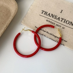 Close-up of elegant red enamel hoop earrings with gold-tone hardware on linen background
