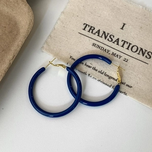 Detail of dark blue enamel hoop earring with gold closure on textured background