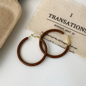 Macro shot of large brown resin hoop earrings with gold-tone metal clasp on rustic fabric