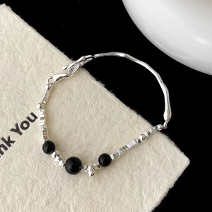 Macro di un bracciale minimalista in argento con perle nere e barra in metallo ondulata