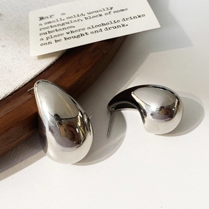 Close-up of silver teardrop stud earrings with a polished mirror finish on a texture base