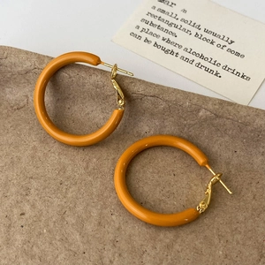 Detail von tiefroten Emaille-Creolen mit Gold-Finish auf vintage Papier-Hintergrund