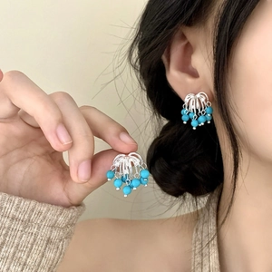 Detailed view of silver fireworks tassel earrings with light blue beads on a model