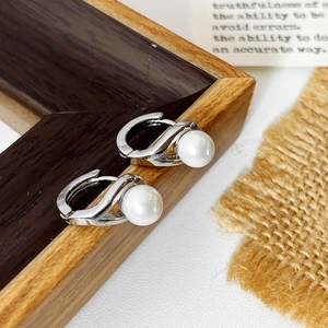 Close-up of elegant S-shape silver pearl hoop earrings on a minimalist rustic background