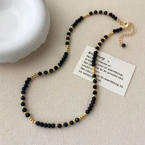 Detail of black crystal beaded necklace with gold spacers on minimalist fabric