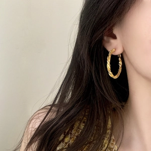 Elegant gold twisted hoop earrings with woven texture on a model in a side view profile