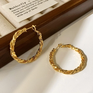 Macro detail of golden twist hoop earrings with textured spiral design on jewelry box
