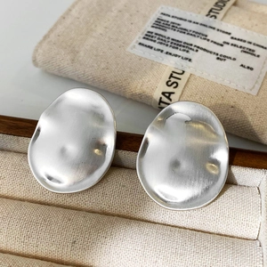 Close-up of matte brushed silver irregular oval earrings in a luxury jewelry box