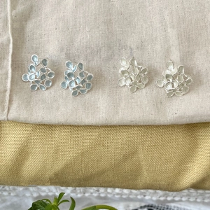 Detail of floral earrings in light blue and cream white with enamel petals on linen background