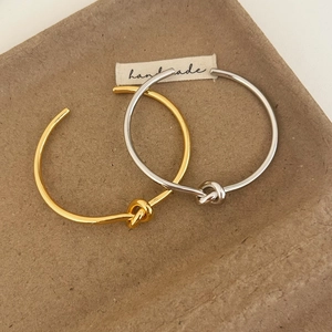 Minimalist knotted open cuff bracelets in polished gold and silver finishes on a tray