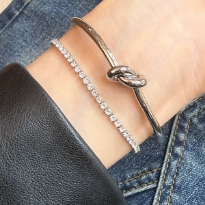 Silver knot bangle and sparkling tennis bracelet set styled on wrist with denim and leather