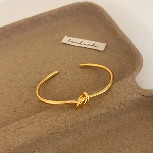 Detail of a handmade gold knot cuff bracelet on a minimalist textured paper tray