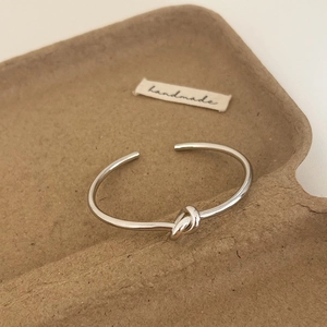 Macro shot of silver minimalist knot cuff bracelet in eco-friendly paper packaging