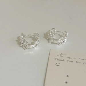 Detail of silver hoop earrings featuring intricate hollow leaf patterns and secure clasp