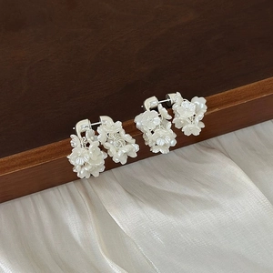 Eleganti orecchini a fiore bianco con nappe e petali di conchiglia su sfondo di seta