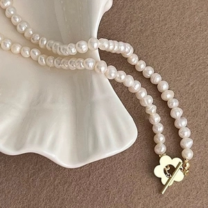 Elegant freshwater pearl necklace with a golden flower toggle clasp on ceramic tray