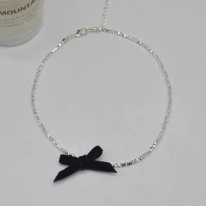 Close-up of silver beaded necklace with a black velvet bow pendant and adjustable lobster clasp