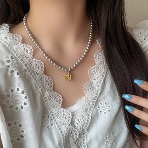 Collier élégant en perles grises avec pendentif fleur dorée sur le cou d'un modèle