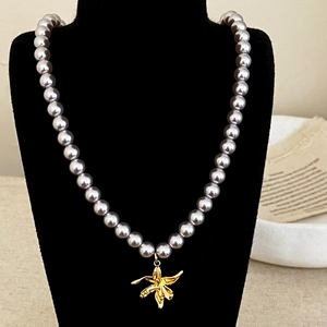 Détail d'un collier de perles gris-violet avec pendentif orchidée dorée sur buste noir