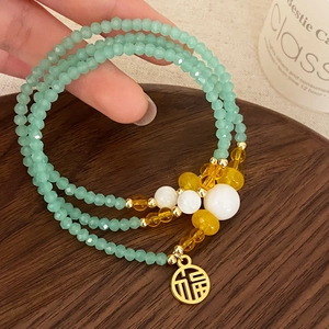 Three-layer green crystal bead bracelet with a gold Fu pendant on a wooden tray