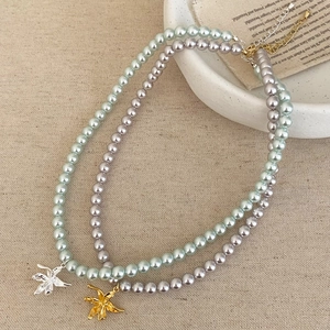 Détail de colliers de perles avec pendentif lys, fermoir mousqueton et chaîne d'extension