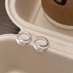Minimalist matte silver cross S-shaped earrings on a textured tray in a cozy lifestyle setting