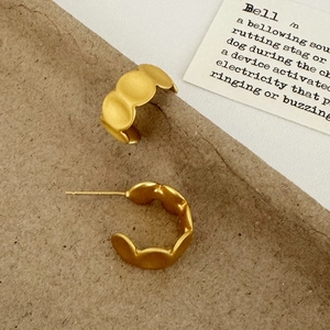 Dettaglio di orecchini a C in oro opaco con trama ondulata su sfondo vintage