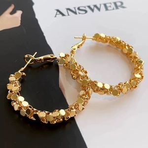 Detail of gold hoop earrings with textured hexagonal honeycomb particles on the surface