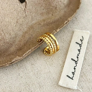 Detail of gold triple-layered ear cuff with beaded texture on textured paper