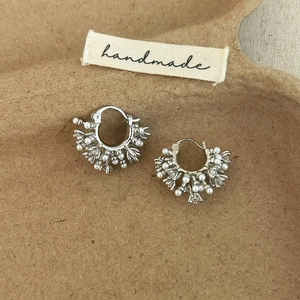 Macro detail of silver pearl hoop earrings with clustered crystals on a rustic base