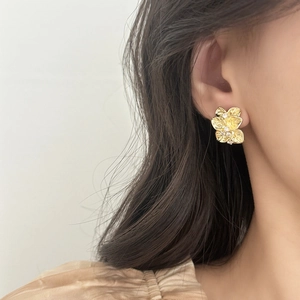 Elegant gold flower stud earrings with brushed metal petals and zircon centers on model