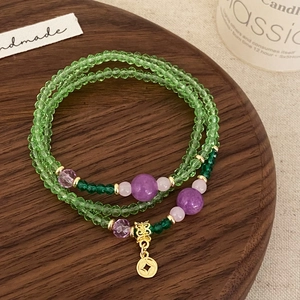 Détail d'un bracelet multicouche avec cristaux verts et pendentif en forme de pièce dorée