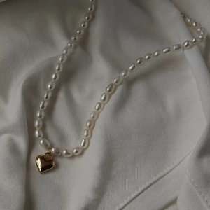 Elegant freshwater pearl necklace with a polished gold heart pendant on white fabric