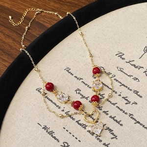 Détail du collier doré double couche avec pendentif cœur en zircone et perles rouges