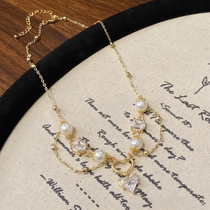 Détail du collier doré multicouche avec zircons en cœur et perles sur tissu poétique