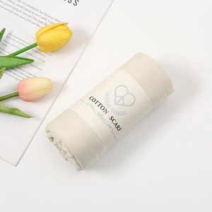 Minimalistische beige katoenen sjaal opgerold met een papieren merkband