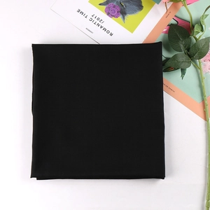 Close-up of black solid color square hijab scarf folded neatly on a white surface