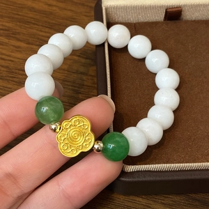 Vue à main d'un bracelet en perles de jade blanc avec breloque nuage dorée élégante