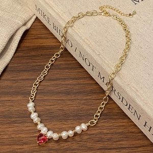 Détail d'un collier doré avec perles d'eau douce et pendentif cœur rouge sur bois