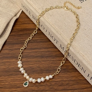 Détail d'un collier doré élégant avec perles et pendentif en pierre verte en goutte