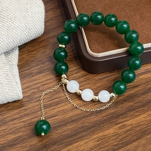 Macro detail of green agate beaded bracelet with white jade beads and gold tassel accents
