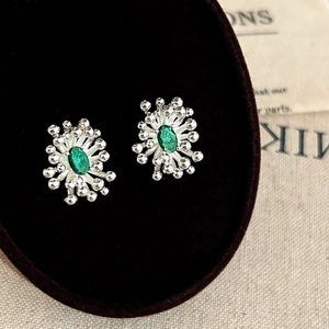 Detailed macro shot of irregular fireworks stud earrings with emerald green gemstones
