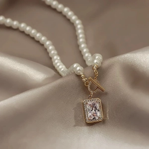 Elegant pearl necklace with cubic zirconia pendant and OT clasp on champagne silk background